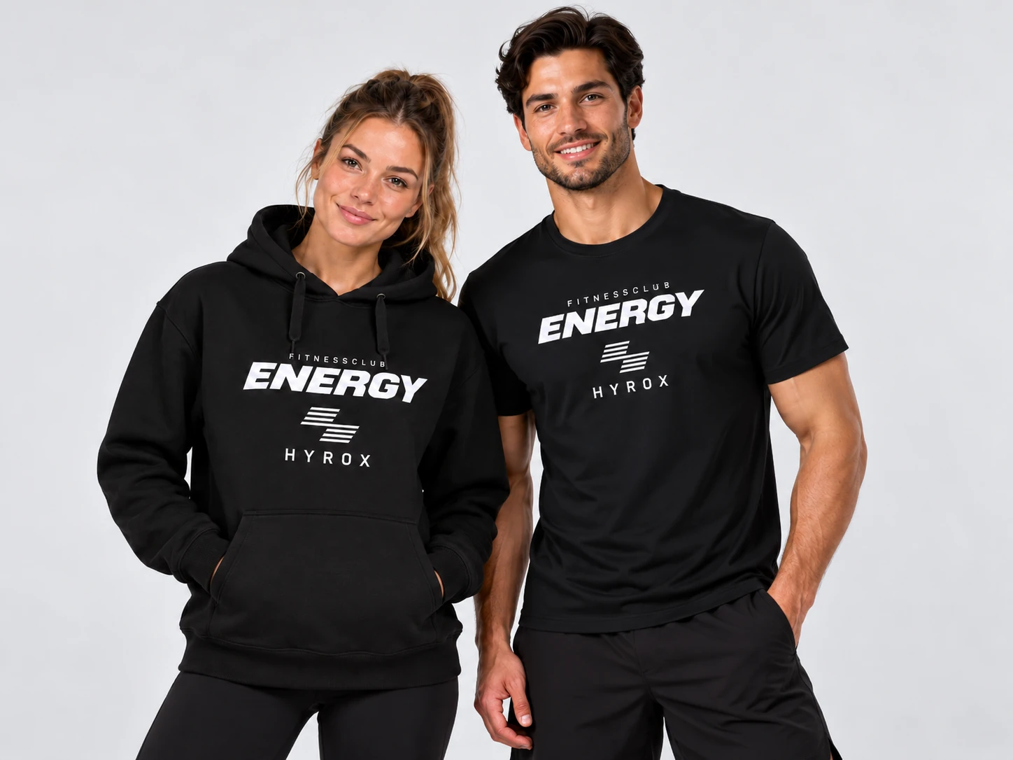 Dame in zwarte Fitnessclub Energy HYROX-hoodie en heer in zwart HYROX T-shirt, samen gefotografeerd voor de Energy Clubshop