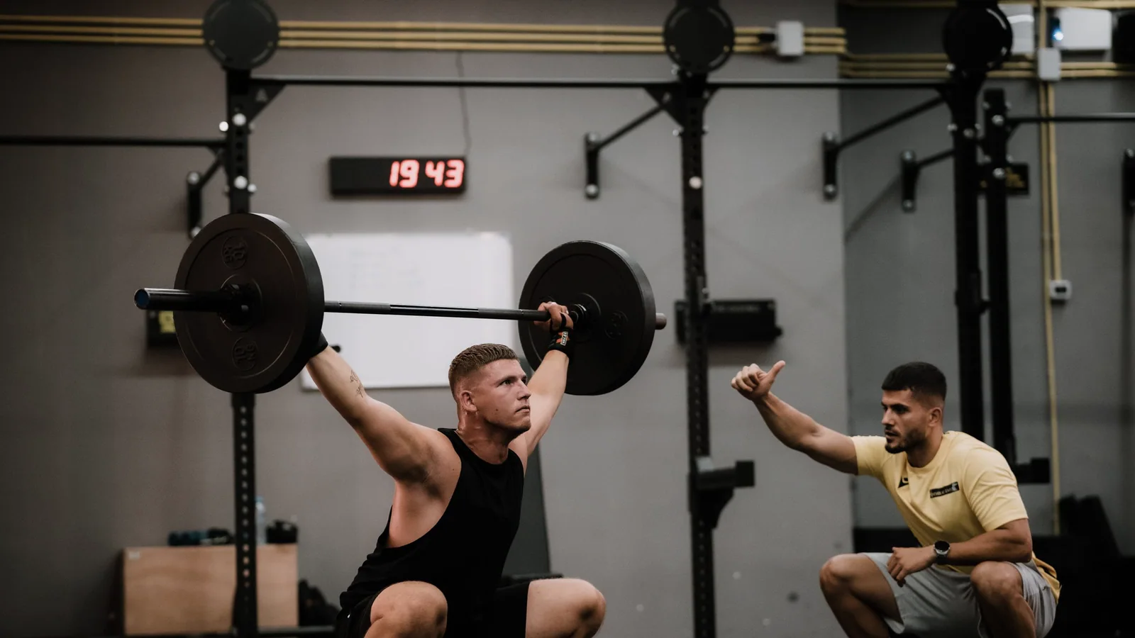 Fitnesscoach helpt een sporter bij een squat met een halter in de sportschool